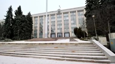 View of government building during a snowfall in Chisinau, Moldova. Flag, stairs, firs