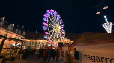 ROMANIA, SIBIU - DECEMBER, 2022: View of the Historic Centre of the town with Christmas fair. The Great Square decorated with ferris wheel, illumination, old buildings and multiple people