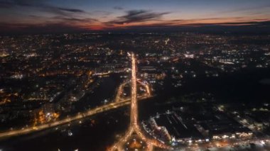 Aerial drone timelapse view of Chisinau at sunset, Moldova. View of the city with multiple buildings, lake, roads with traffic, illumination