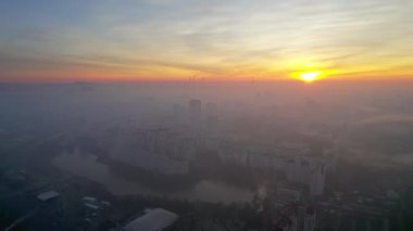 Aerial drone view of Chisinau at sunrise, Moldova. View of the city with fog in the air, multiple buildings, roads, lake, bare trees