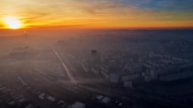 Aerial drone timelapse view of Chisinau at sunrise, Moldova. View of the city with fog in the air, multiple buildings, roads, lake, bare trees