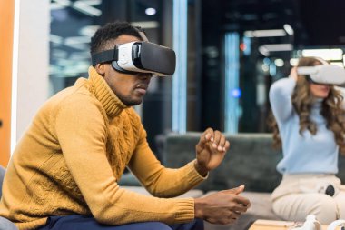 A black man exploring virtual reality using VR glasses in an office