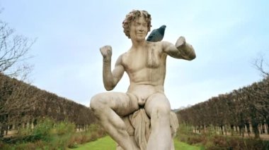 View of a sculpture in Gardens of the Palais-Royal in Paris downtown, France. Walking people, bare trees, cloudy weather
