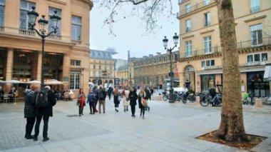 PARIS, FRANCE - JANUARY, 2022: Street view of the city downtown. Classic buildings, walking people, Mirror Cube art installation and Louvre Palace, cloudy weather