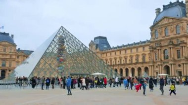 PARIS, FRANCE - JANUARY, 2022: View of the Louvre from the Napoleon Courtyard. Louvre Palace, Pyramid with a long queue inside, a lot of tourists, cloudy weather