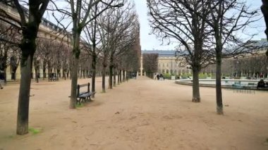 PARIS, FRANCE - JANUARY, 2022: View of Gardens of the Palais-Royal in city downtown. Walking people, bare trees, fountain, cloudy weather