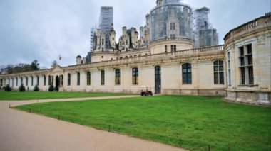 View of the Chateau de Chambord exterior with illuminated trees and people in front of it at cloudy weather, France