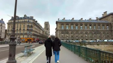 PARIS, FRANCE - DECEMBER, 2022: Street view of city downtown. People walking on a bridge, classic buildings, Notre-Dame de Paris in the distance