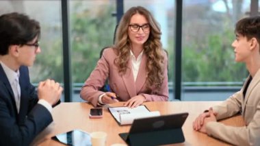Business meeting in an office, female team leader and two young men discussing business affairs using gadgets and notebook. Shaking hands