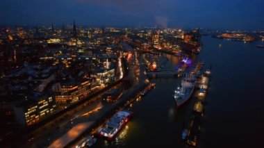 Aerial drone view of Hamburg at evening, Germany. Elbe coastline, moored boats, sea port, classic and modern buildings, roads with cars and nightlights