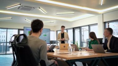 Young worker leading business meeting in an office, discussing business affairs with other workers using a big display with info