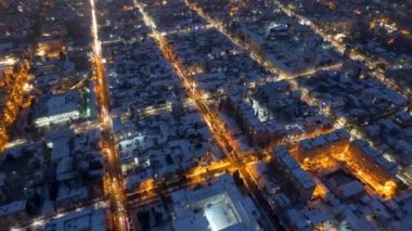 Aerial drone timelapse view of Chisinau at sunset in winter, Moldova. View of the city with multiple buildings and roads covered with snow, moving cars, illumination