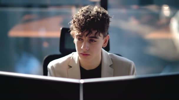 若い男がオフィスのコンピュータで働いている背景の窓 — ストック動画