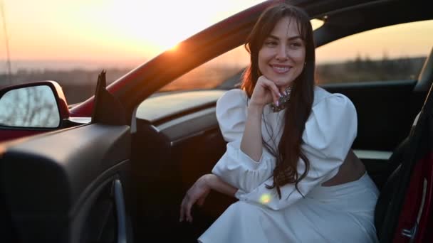 Ευτυχισμένη Γυναίκα Λευκό Φόρεμα Ένα Κόκκινο Αυτοκίνητο Στο Ηλιοβασίλεμα — Αρχείο Βίντεο