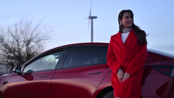 Boldog Pózol Egy Piros Autó Szélturbina Közelében Naplementekor — Stock videók