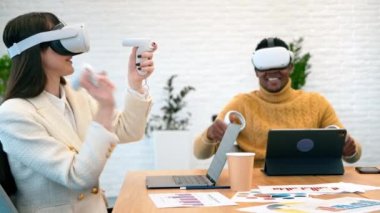 Business conference in VR in an office. A black man and caucasian woman using VR glasses and controllers, papers and gadgets on the table