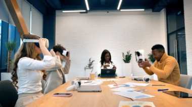 Business conference in VR in an office. Multiracial group of people using VR glasses and controllers, papers and gadgets on the table
