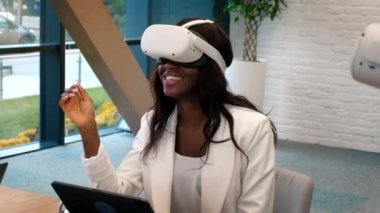 VR 'da bir ofiste iş konferansı. Siyah bir adam ve kadın VR gözlük ve kumanda kullanıyor. Tablet masada.