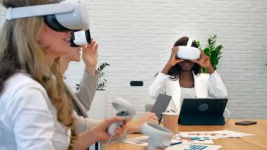 Business conference in VR in an office. Multiracial group of people using VR glasses and controllers, papers and gadgets on the table