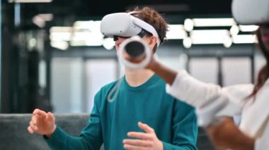 Ofiste VR gözlüklerini çıkaran genç, heyecanlı bir beyaz adam ve yakınlarda VR gözlüklü diğer insanlar.
