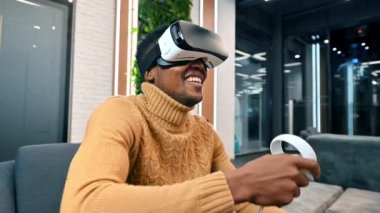 Sanal gerçekliği keşfeden siyah bir adam bir ofiste VR gözlükleri ve kumandalar kullanıyor.