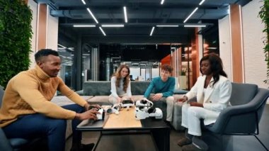 VR 'da bir ofiste iş konferansı. Çok ırklı bir grup insan VR gözlük ve kumanda takıyor.