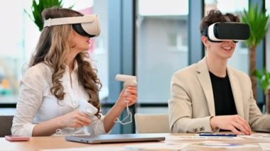 VR 'da bir ofiste iş konferansı. Kafkas bir kadın ve genç bir adam VR gözlük ve kumanda kullanıyor. Masada aletler var. Yavaş çekim
