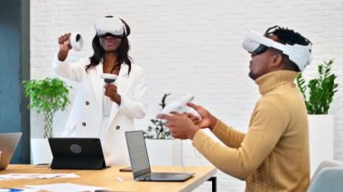 VR 'da bir ofiste iş konferansı. Siyah bir adam ve kadın VR gözlük ve kumanda kullanıyor. Masada aletler var. Yavaş çekim