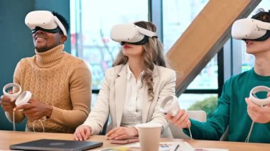 VR 'da bir ofiste iş konferansı. Sanal gerçeklik gözlüğü, kumanda, kâğıt ve aletleri kullanan çok ırklı bir grup insan masanın üzerinde. Yavaş çekim