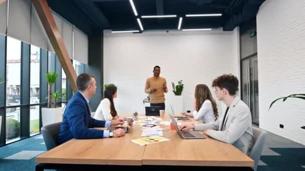 オフィスでのビジネスミーティングで黒人男性チームリーダー テーブルの上に他の労働者とのビジネス問題を議論 紙やガジェット — ストック動画