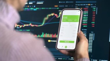 Açılmış kredi başvurusu ile akıllı telefonu elinde tutan kişinin yakın görüntüsü. Arkaplanda hisse senedi çizelgeleri