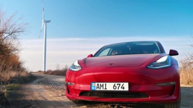 CHISINAU, MOLDOVA - Şubat 2023: park halindeki Tesla Model 3. Arka planda rüzgar türbini