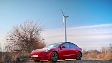 CHISINAU, MOLDOVA - Şubat 2023: park halindeki Tesla Model 3. Arka planda rüzgar türbini