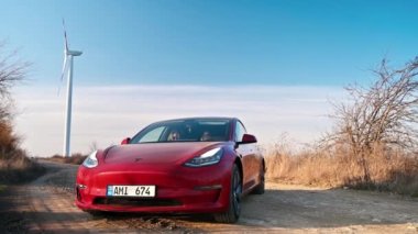 CHISINAU, MOLDOVA - Şubat 2023: park halindeki Tesla Model 3. Arka planda rüzgar türbini