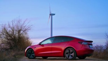 CHISINAU, MOLDOVA - Şubat 2023: park halindeki Tesla Model 3. Gün batımında arka planda rüzgar türbini