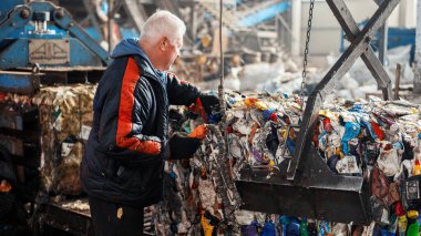 CHISINAU, MOLDOVA - Mart 2023: Bir çalışan atık toplama tesisinde bir yükleyici kullanarak sıkıştırılmış çöp yığıyor