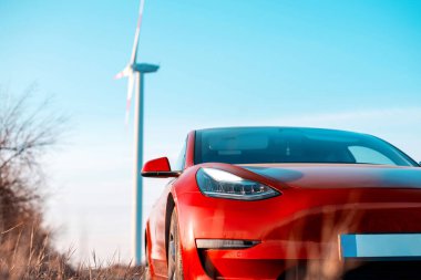 Park halindeki kırmızı elektrikli arabanın görüntüsü. Arka planda rüzgar türbini