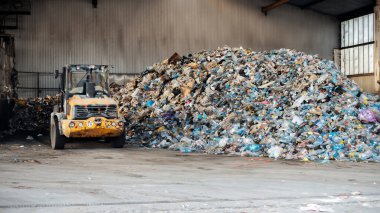 Yakındaki atık tasnif tesisinde büyük bir plastik çöp yığını ve kazıcı görüntüsü