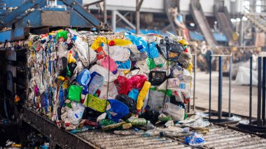 Atık tesisinde bir taşıyıcı bandında sıkıştırılmış plastik çöp küpü