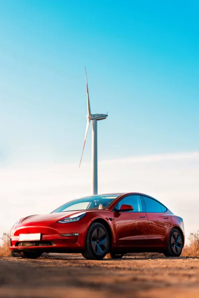 Widok Zaparkowanego Czerwonego Samochodu Elektrycznego Turbina Wiatrowa Tle — Zdjęcie stockowe