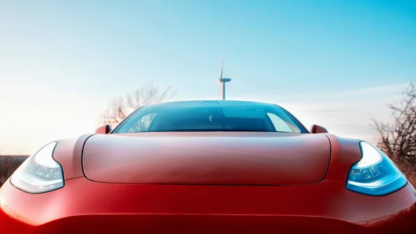 Zavřít Přední Pohled Zaparkované Červené Elektrické Auto Větrná Turbína Pozadí — Stock fotografie