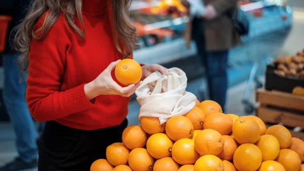 店内の再利用可能な袋にオレンジを選ぶ女性 生態学と地球の日のテーマ — ストック写真