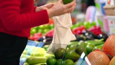 Mağazada tekrar kullanılabilir bir çantada avokado toplayan bir kadın. Ekoloji ve Dünya Günü teması