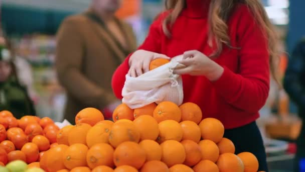 店内の再利用可能な袋にオレンジを選ぶ女性 生態学と地球の日のテーマ — ストック動画
