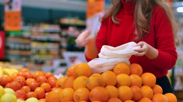 店内の再利用可能な袋にオレンジを選ぶ女性 生態学と地球の日のテーマ — ストック動画