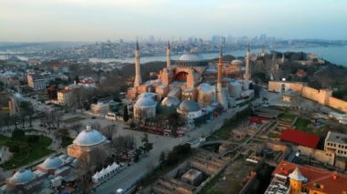 Türkiye 'de gün batımında İstanbul' un hava aracı görüntüsü. Önünde bahçeler olan Ayasofya, arka planda Boğaz ve şehir manzarası, etrafındaki binalar.