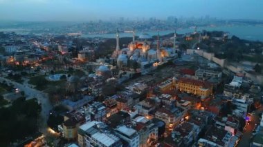 Türkiye 'de gün batımında İstanbul' un hava aracı görüntüsü. Önünde bahçeler olan Ayasofya, arka planda Boğaz ve şehir manzarası, etrafındaki binalar.