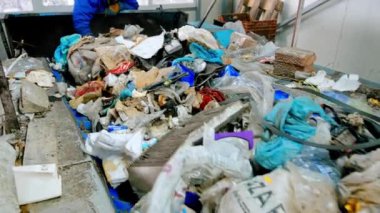 Atık tasnif tesisinde çöp taşıyıcı bant üzerinde çalışan bir çalışan