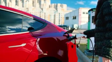 CHISINAU, MOLDOVA - Mart 2023: kırmızı bir Tesla Model 3 'ün şarj aletini söken bir kadının görüntüsü. Yavaş çekim