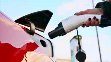 CHISINAU, MOLDOVA - Mart 2023: kırmızı Tesla Model 3 'e şarj aleti takan bir kadının yakın görüntüsü. Yavaş çekim